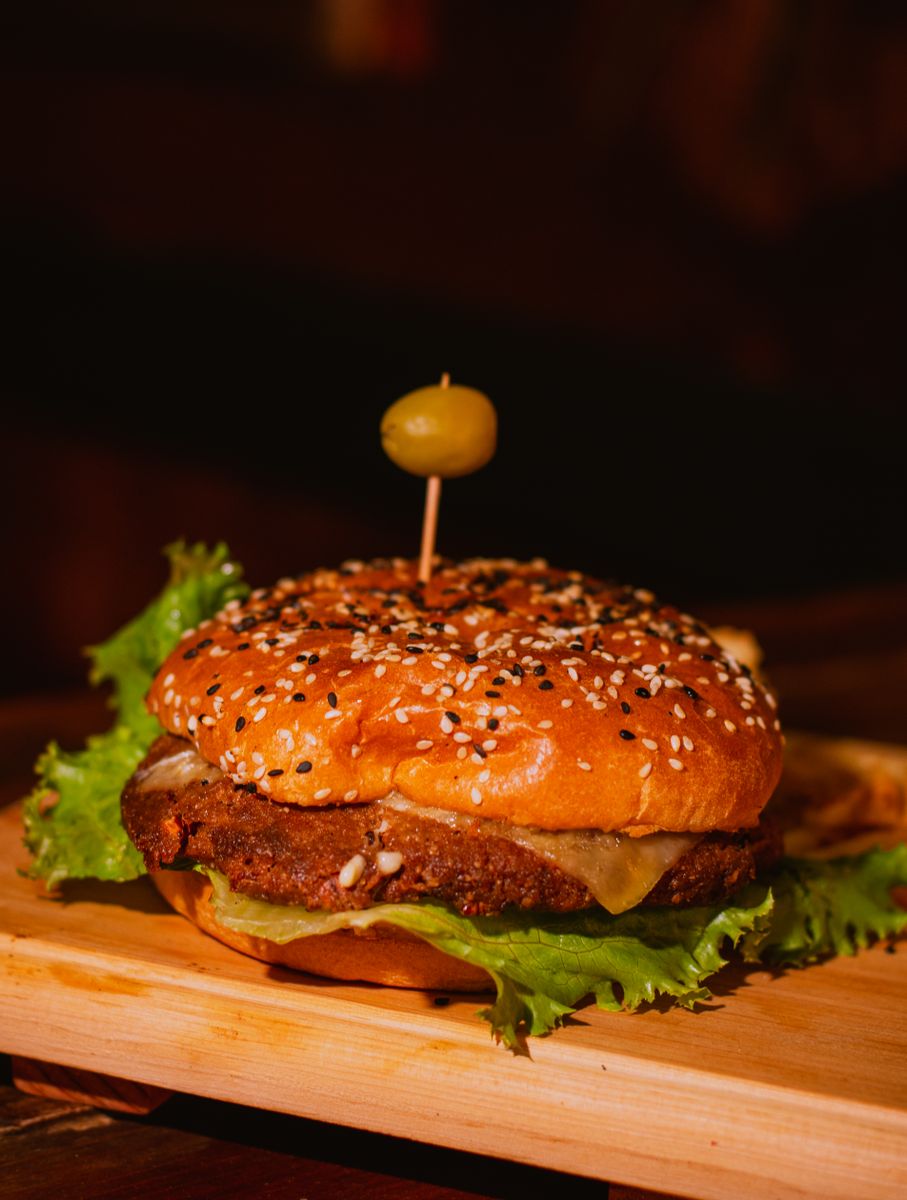 Mouth-watering cheeseburger with sesame seed bun garnished with an olive on a wooden board.