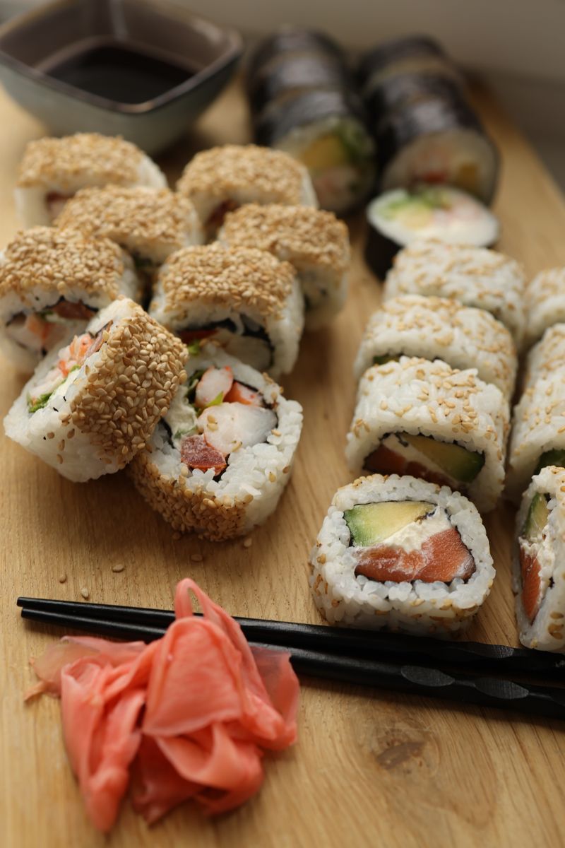 Mouth-watering sushi rolls with various fresh ingredients served on a wooden board with ginger and soy sauce in a restaurant setting.
