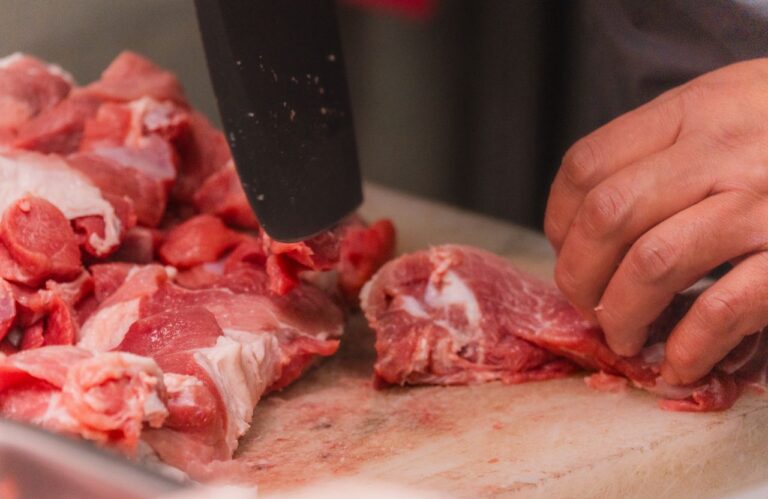 /close-up-of-raw-meat-being-cut-on-chopping-board-