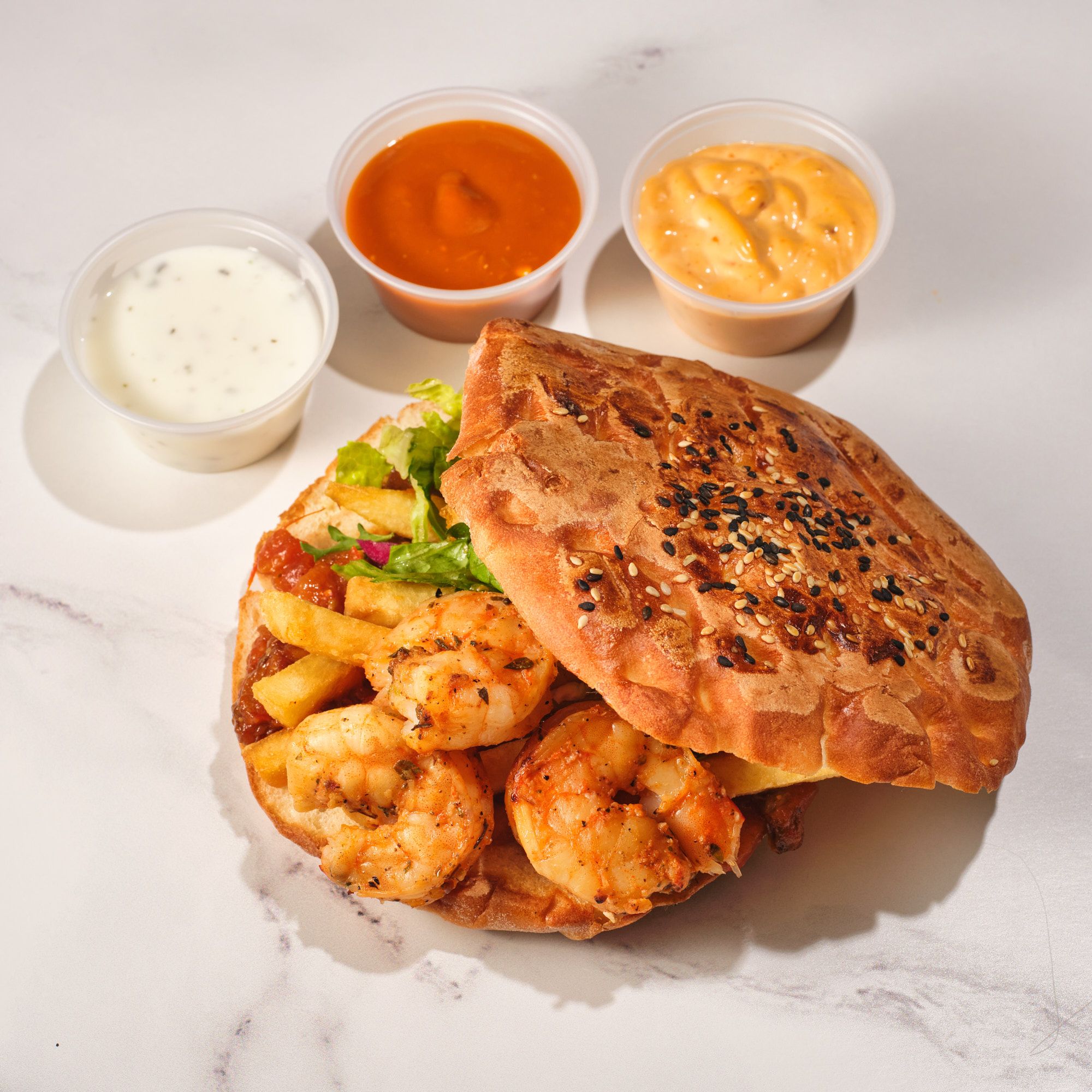 Savor a mouthwatering shrimp po boy sandwich with crispy fries and assorted sauces on a marble surface.