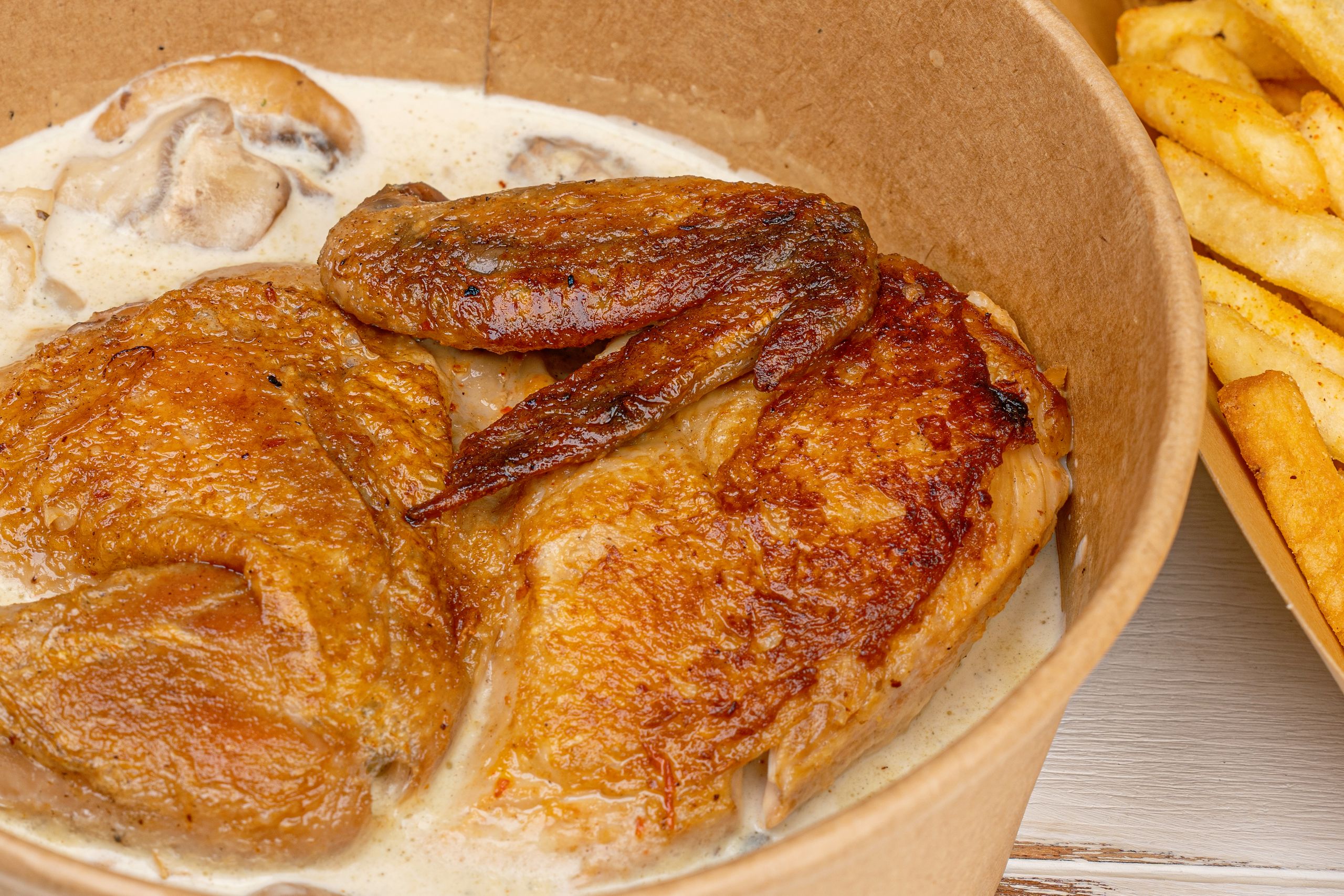 Savory roasted chicken with mushroom sauce in paper bowl, served with fries. Perfect comfort food.