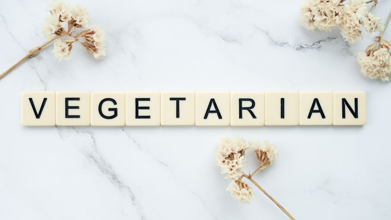 Scrabble tiles spelling 'vegetarian' on a marble surface with dried flowers.
