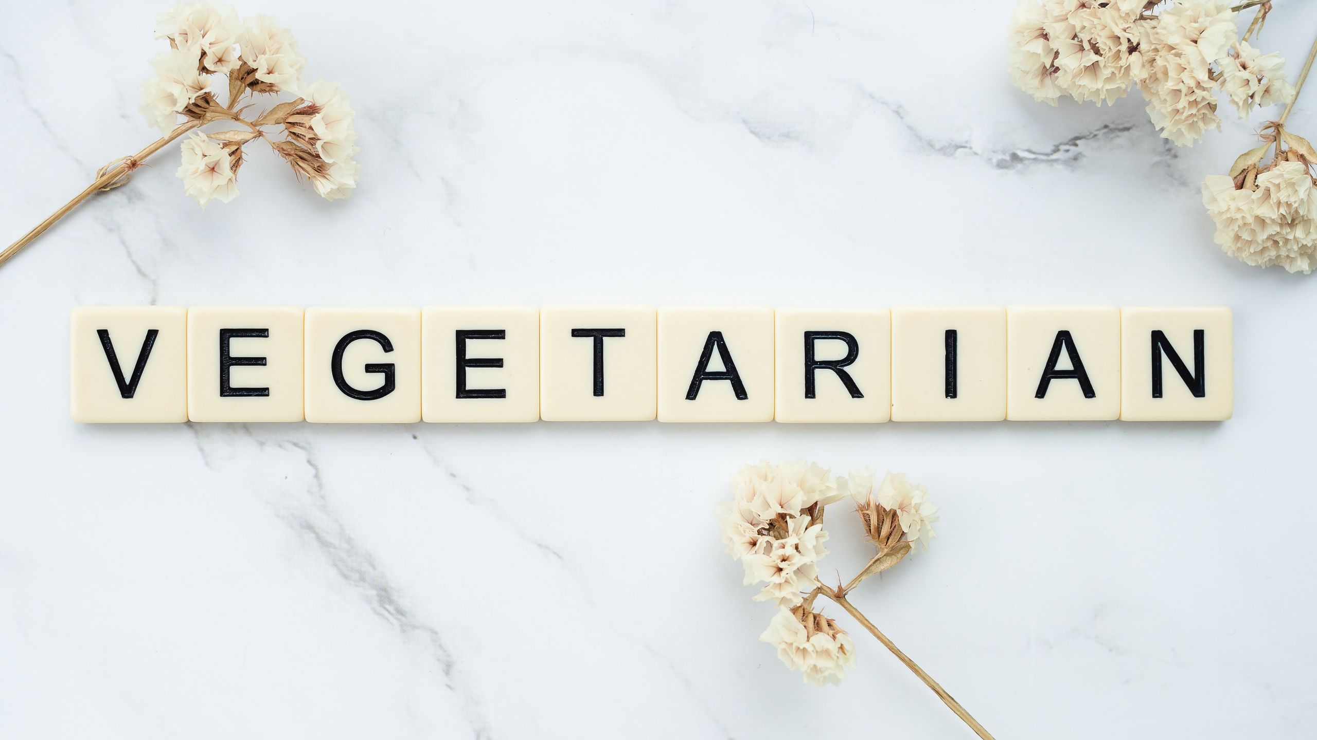 Scrabble tiles spelling 'vegetarian' on a marble surface with dried flowers.