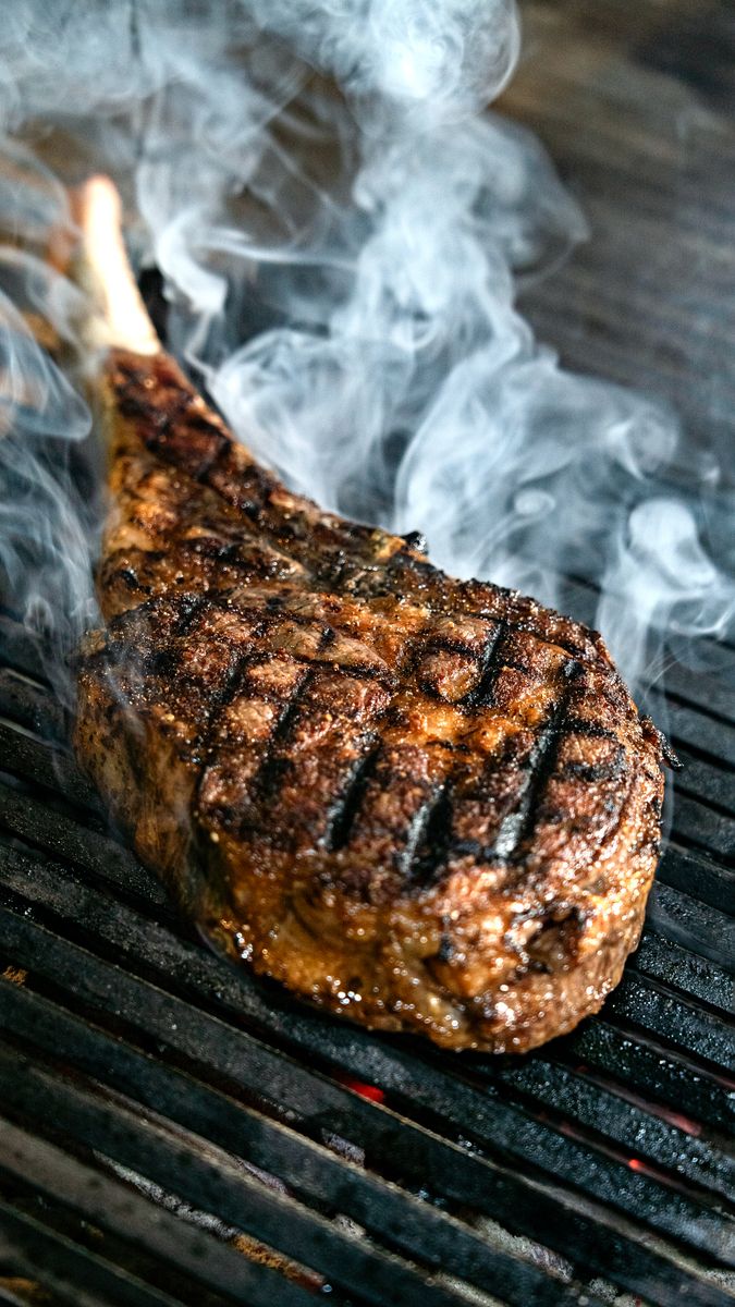 Sizzling tomahawk steak with grill marks and smoke on a barbecue grill, perfect for steak lovers.