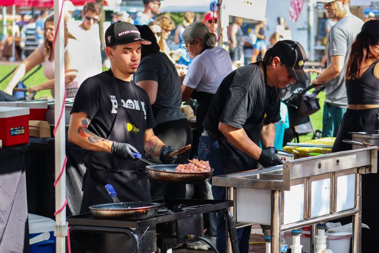 Street vendors preparing meals outdoors at a lively market event on a sunny day.