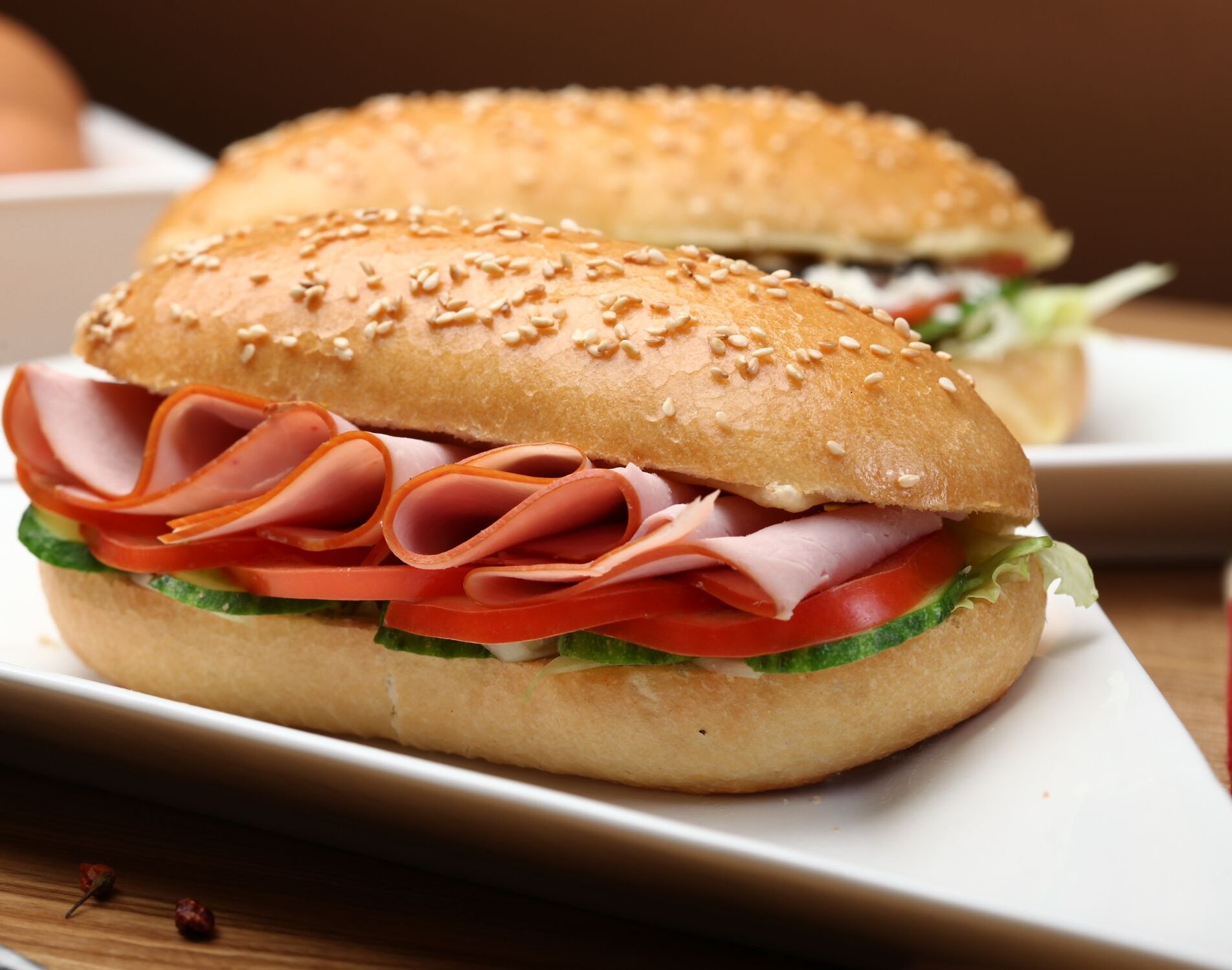 Tasty ham and vegetable sandwich on sesame bun with fresh ingredients served on a white plate.