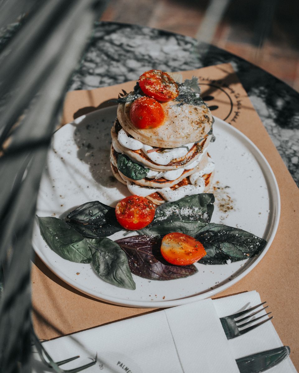 Tasty pancake stack topped with tomatoes and spinach on a plate under sunlight.