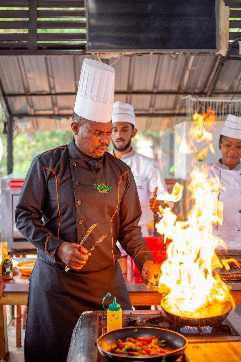 Three chefs in Uganda working with open flames in an outdoor kitchen.