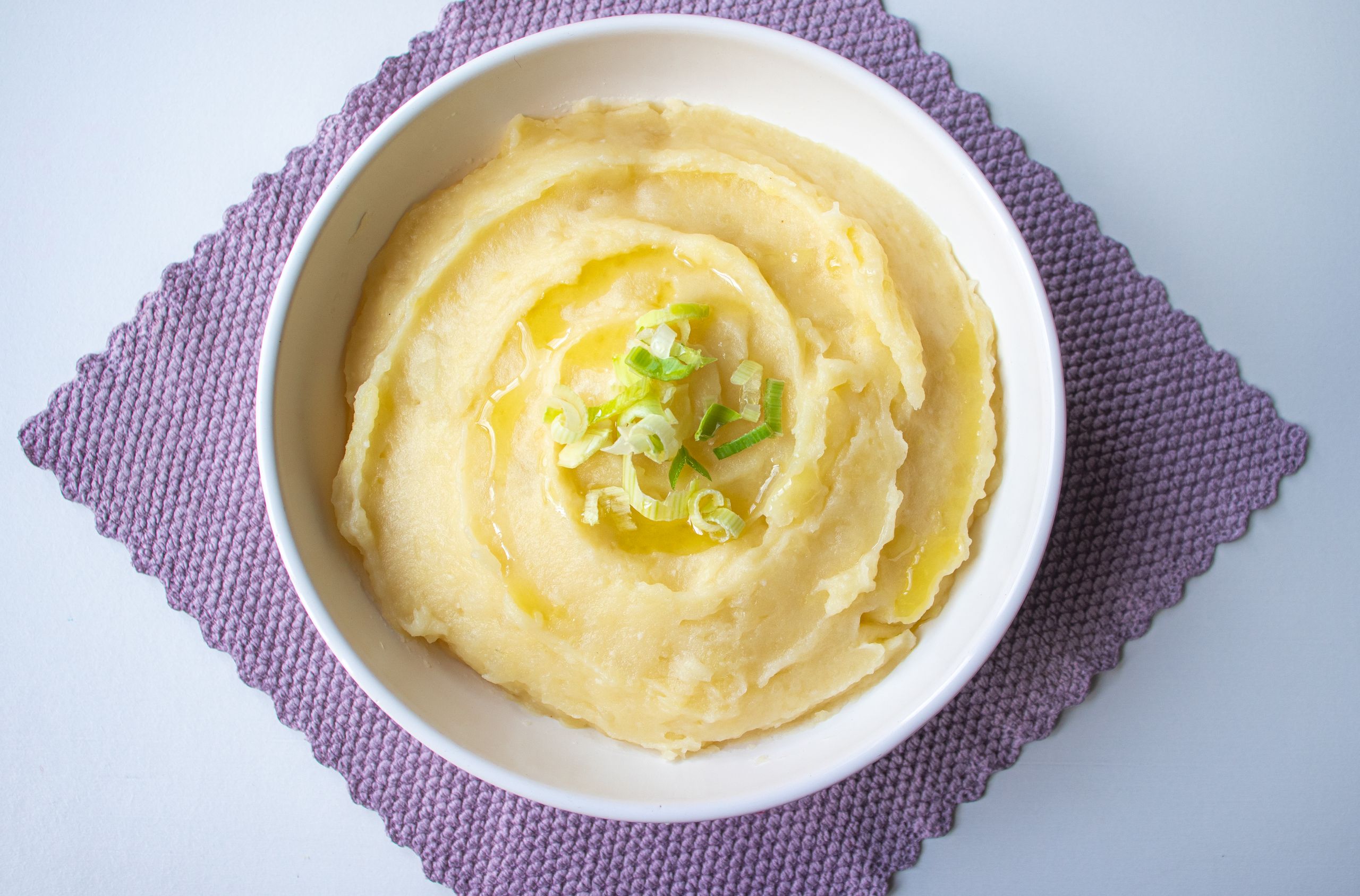 Top-down view of creamy mashed potatoes garnished with scallion in a white bowl.