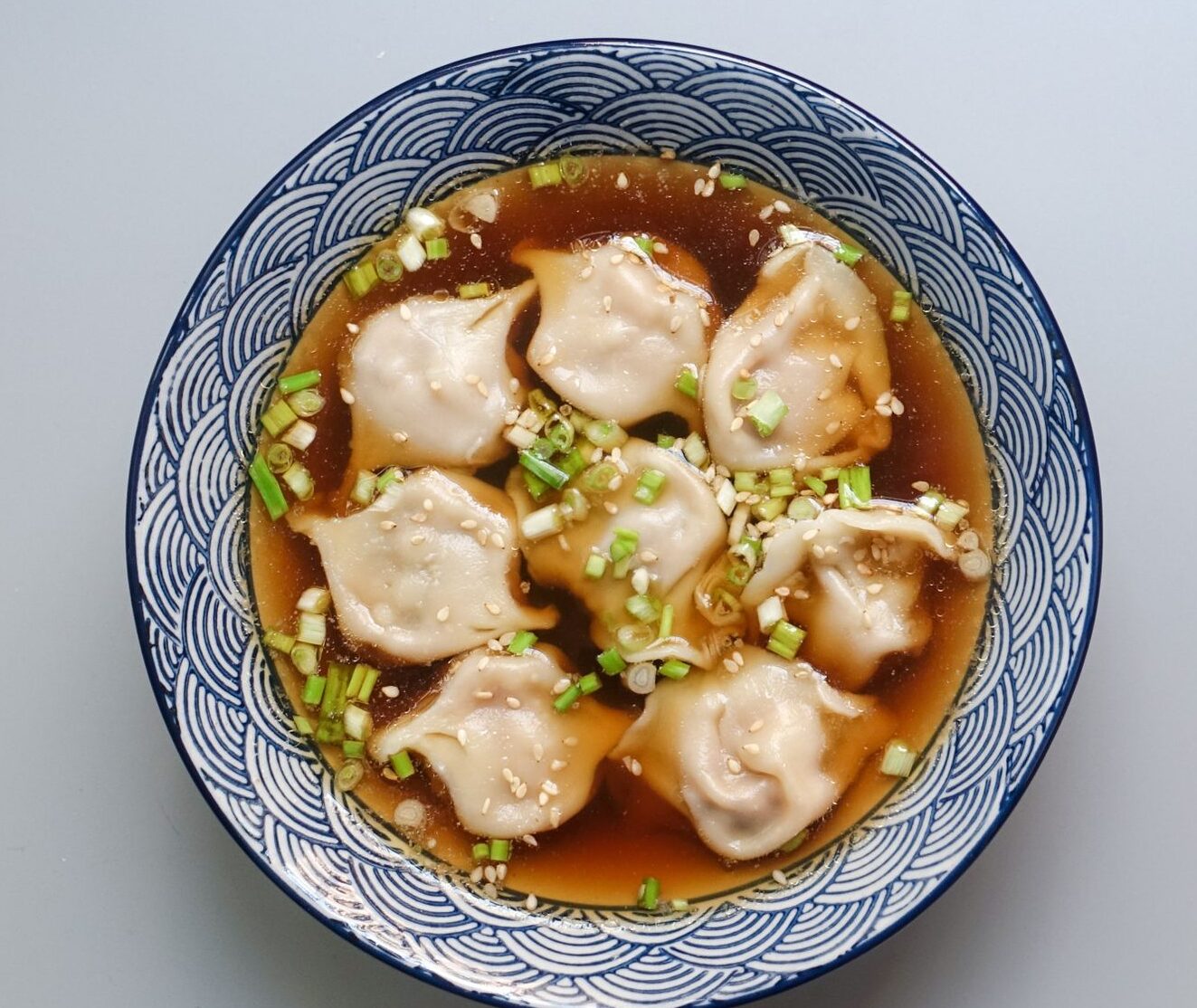 Top view of a bowl of dumplings in soup garnished with scallions.