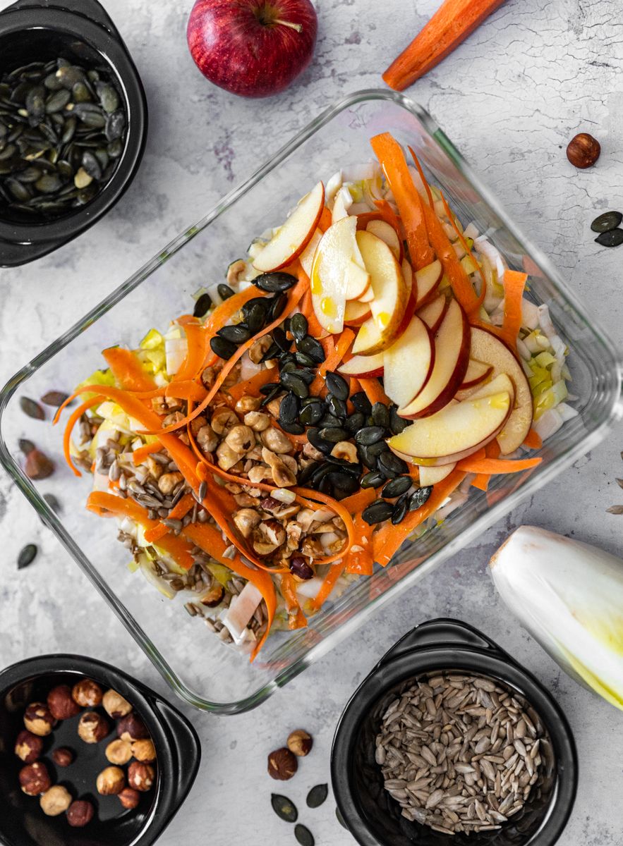 Top view of a fresh salad with apples, carrots, nuts, and seeds.