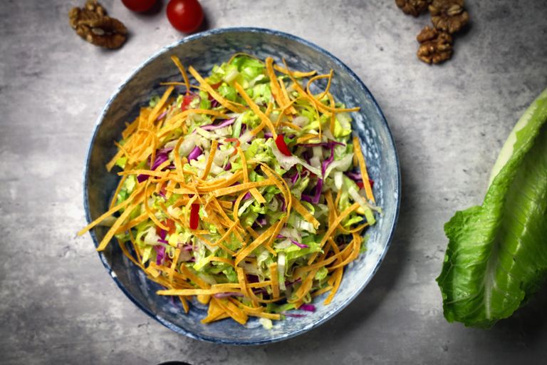 Top view of a vibrant vegetable salad in a blue bowl with fresh ingredients around.
