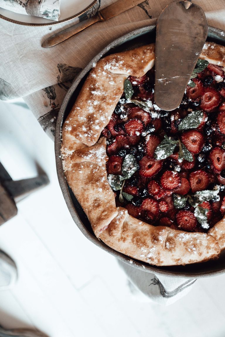 Top view of crostata with strawberry slices and black currants with mint leaves and powdered sugar in baking dish