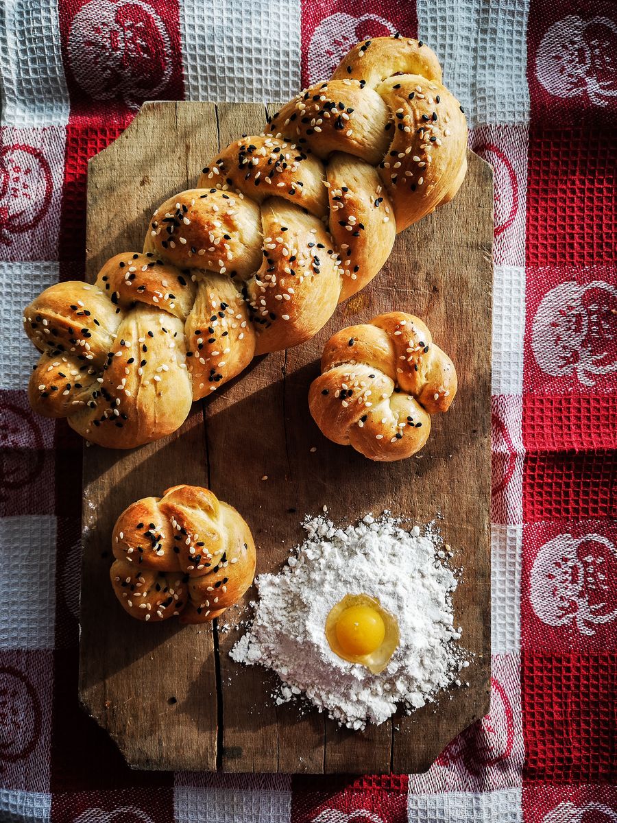Top view of homemade sesame challah bread on a rustic cutting board with flour and egg yolk. Perfect for baking enthusiasts.