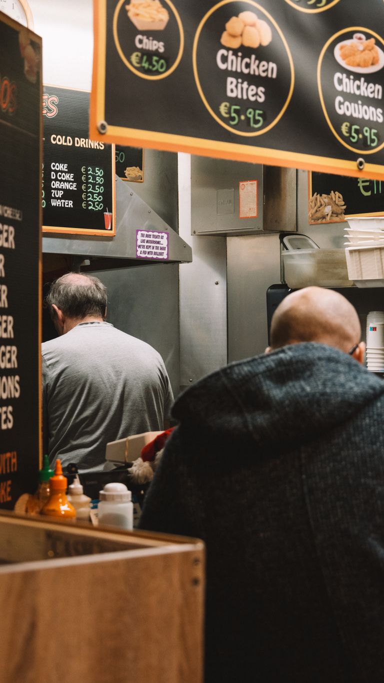 Two adults in a casual eatery with visible menu signs, ordering food.