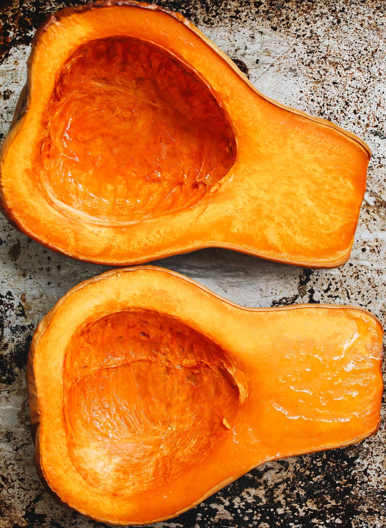 Two halves of roasted butternut squash on a rustic metal tray. Perfect for fall recipes and healthy eating.