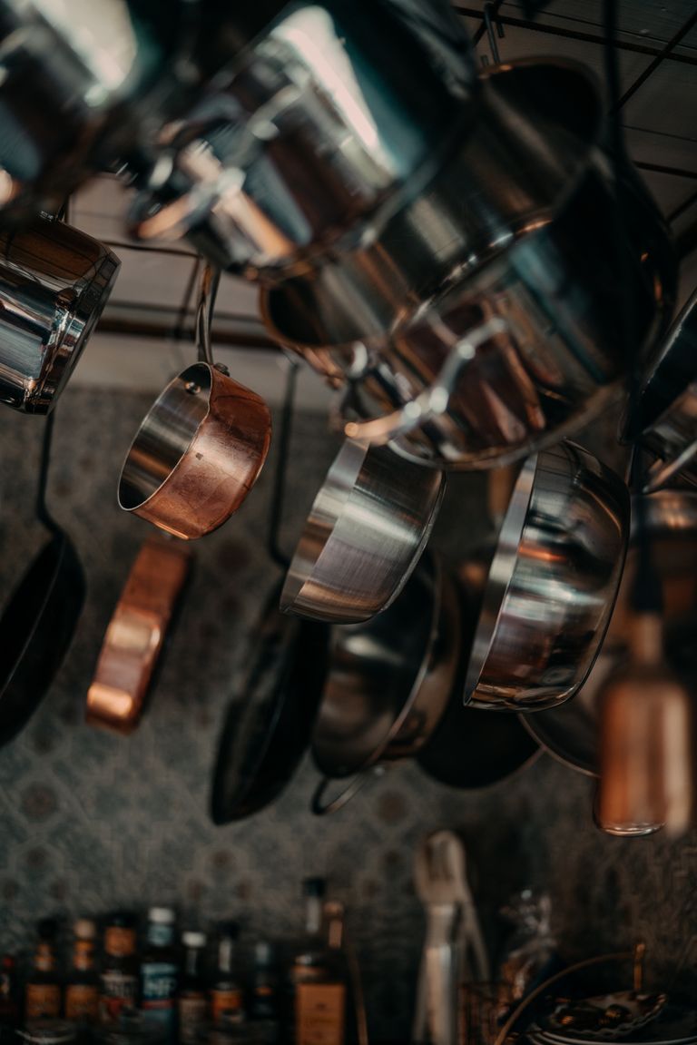Vertical shot of stainless steel and copper pots and pans hanging in a kitchen.