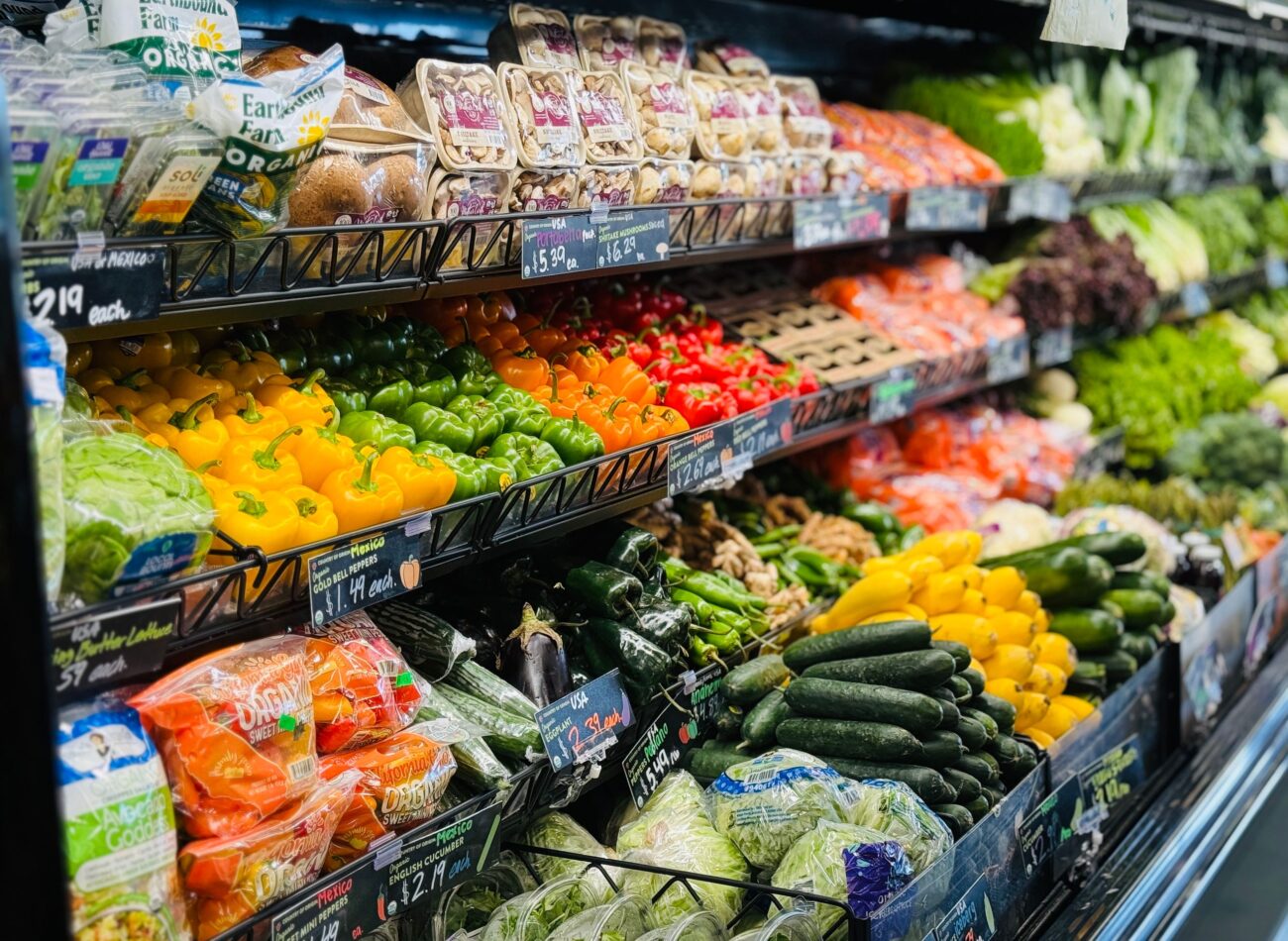 Vibrant variety of fresh vegetables and fruits on grocery store shelves, showcasing healthy choices. Image Credit: Matthew Baxter/Pexels