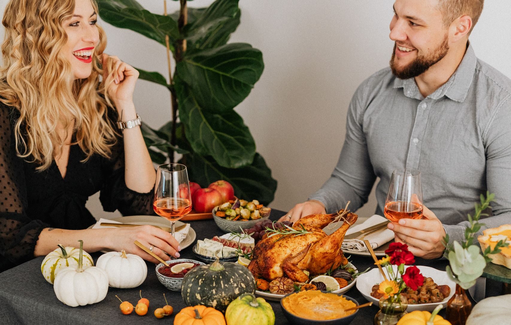 Warm autumn dinner scene featuring a couple with pumpkins, roast chicken, and a pet dog.
